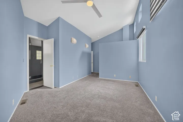 Vaulted ceiling, wall-mounted light fixtures, ceiling fan with integrated lighting, wall-to-wall carpeting, and an entryway to a tiled shower enclosure