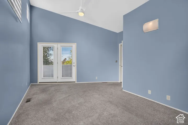 Vaulted ceilings, dual glass-paneled doors, wall-mounted sconce lighting, and a ceiling fan