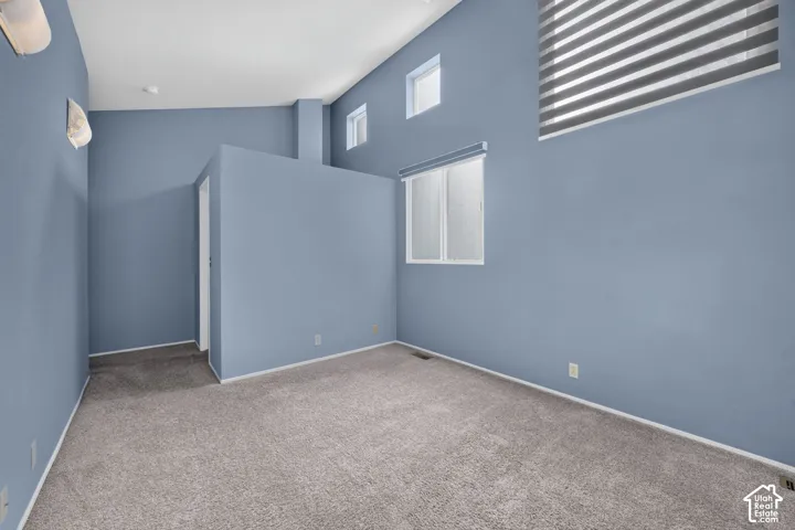 High vaulted ceilings featuring multi-level windows, wall-mounted light fixtures, and wall-to-wall carpeting
