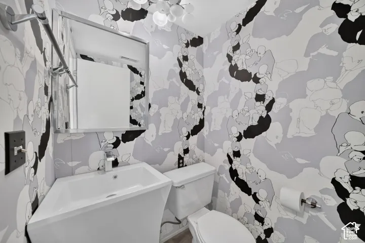 Graphic patterned wallpaper, pedestal sink with chrome faucet, square framed wall mirror, multi-globe light fixture, and chrome towel bar