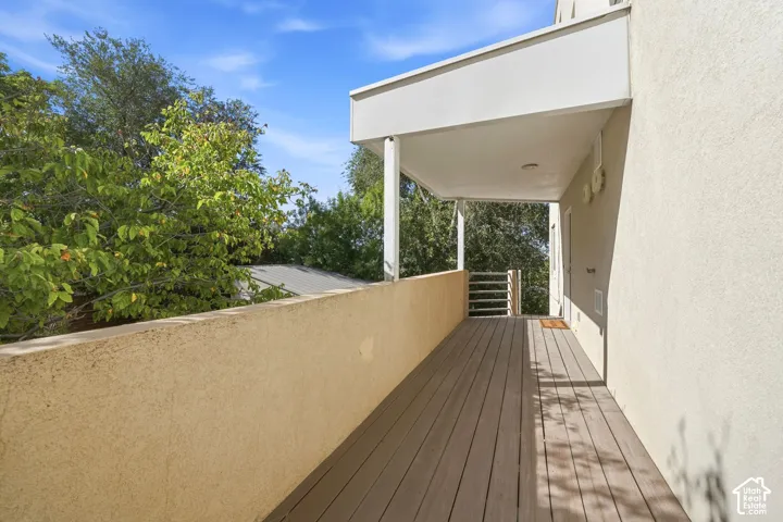Covered balcony featuring wood-finish decking, stucco perimeter wall, and horizontal metal railing
