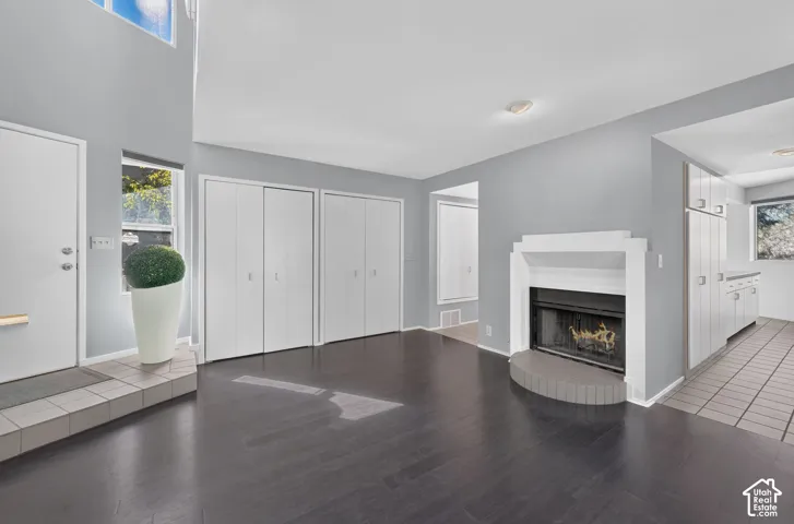High-ceiling living area featuring wood-finish flooring, a fireplace with a stepped mantel, tile entryway flooring, and built-in closet storage
