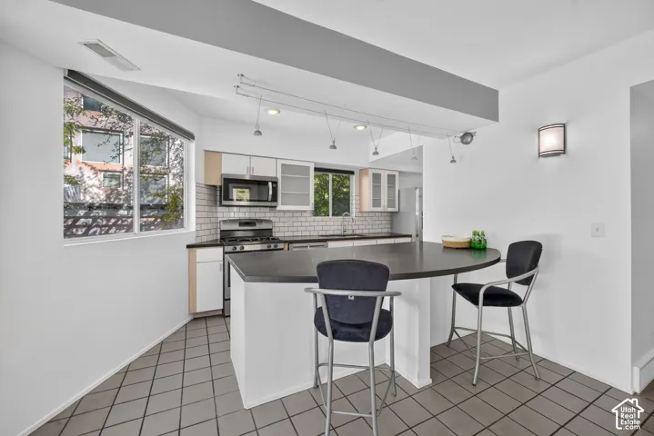 Kitchen featuring a semi-circular island with a dark countertop, white cabinetry, subway tile backsplash, and ceiling-mounted track lighting
