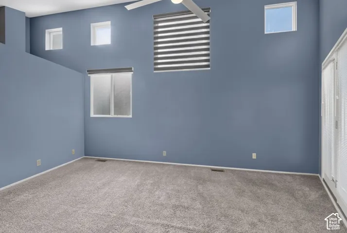 High-ceilinged room featuring wall-to-wall carpeting, multiple windows with integrated shades, and a ceiling fan