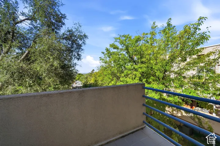 Balcony with tile flooring, solid stucco-finish railing, and blue tubular metal balustrade