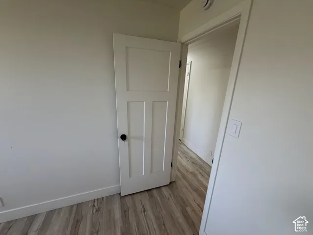 Three-panel shaker-style interior door with matte black hardware, neutral wall paint, and light-tone wood-finish flooring