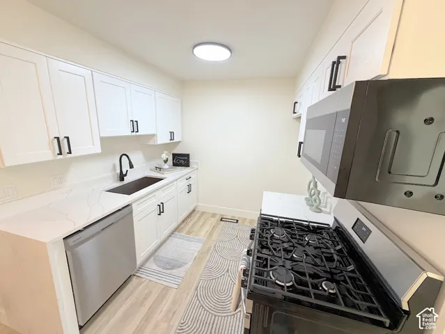 Kitchen featuring white shaker-style cabinetry, white countertops with grey veining, stainless steel gas range, matte black faucet hardware, and wood-finish flooring