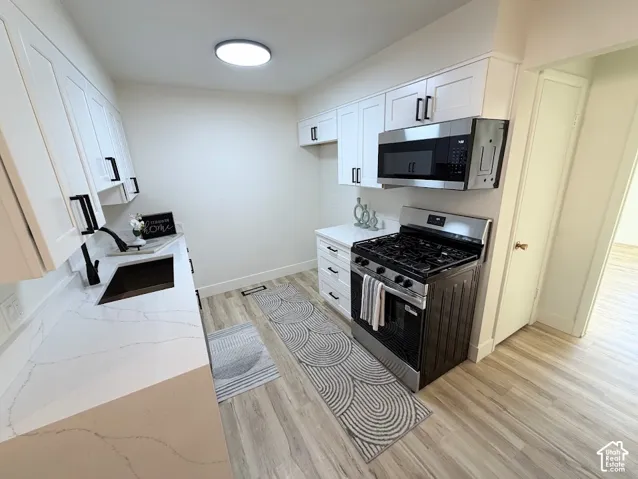 Kitchen featuring white shaker-style cabinetry, quartz countertops, a stainless steel gas range, a matching over-the-range microwave, and light-toned wood-finish flooring