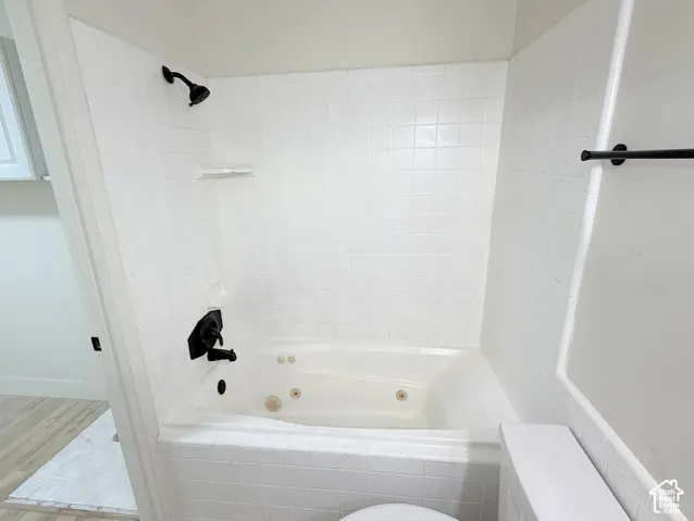 Jetted soaking tub featuring white tile surround, matte black showerhead, and matching matte black wall-mounted faucet