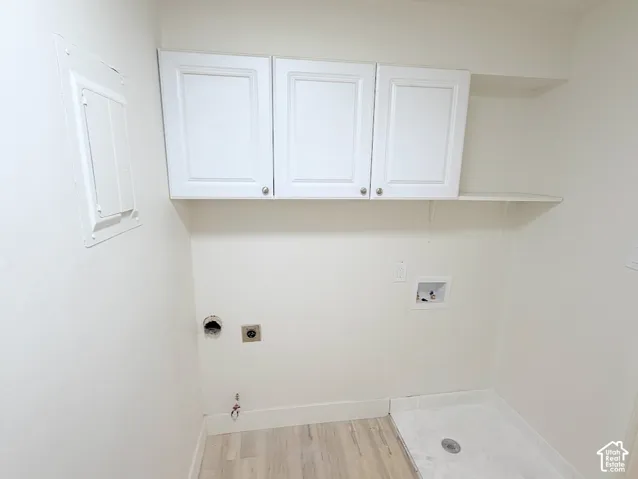 Laundry space featuring white shaker-style wall-mounted cabinetry, integrated shelving, and wood-finish flooring