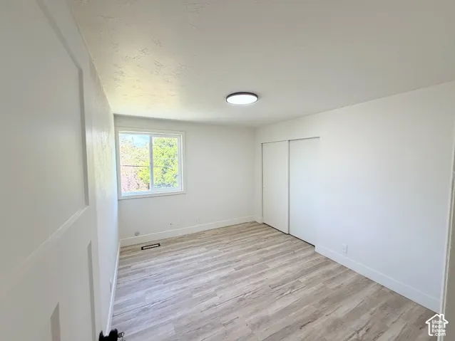 Neutral-toned room featuring wood-finish flooring, a sliding-door closet, a single-pane window, and a flush-mount overhead light fixture