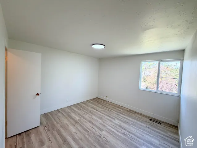 Neutral interior featuring wood-finish flooring, a single-pane window with exterior greenery, a flush-mount ceiling light fixture, and a solid-core interior door