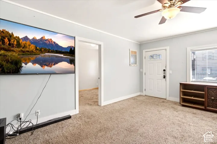 Light-filled room featuring wall-to-wall carpeting, a ceiling fan with integrated lighting, and a white paneled entry door with decorative glass inlay