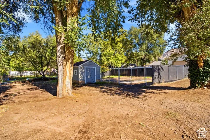 Exterior grounds featuring a detached storage shed, chain-link perimeter fencing, and mature trees