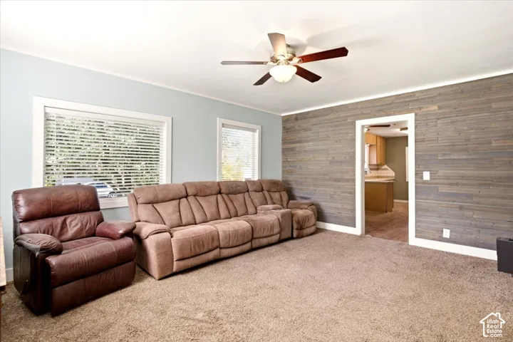 Living area featuring horizontal wood-plank wall paneling, ceiling fan with light fixture, and windows equipped with plantation-style shutters