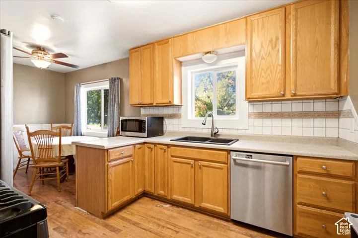 Kitchen featuring wood cabinetry, stainless steel dishwasher, dual-basin sink with arched faucet, tile backsplash, and wood-finish flooring
