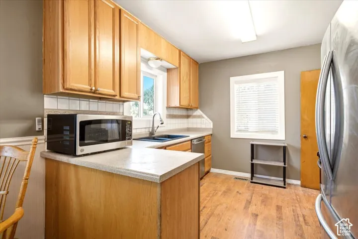 Kitchen featuring wood cabinetry, laminate countertops, a double-basin drop-in sink, integrated dishwasher, and wood-finish flooring