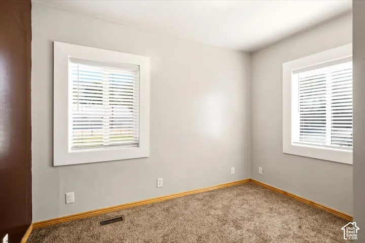 Interior room featuring neutral wall paint, wall-to-wall carpeting, and dual windows with wide-profile white casing