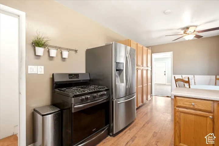 Kitchen featuring stainless steel refrigerator, gas range, wood-finish cabinetry, wood-finish flooring, and ceiling fan