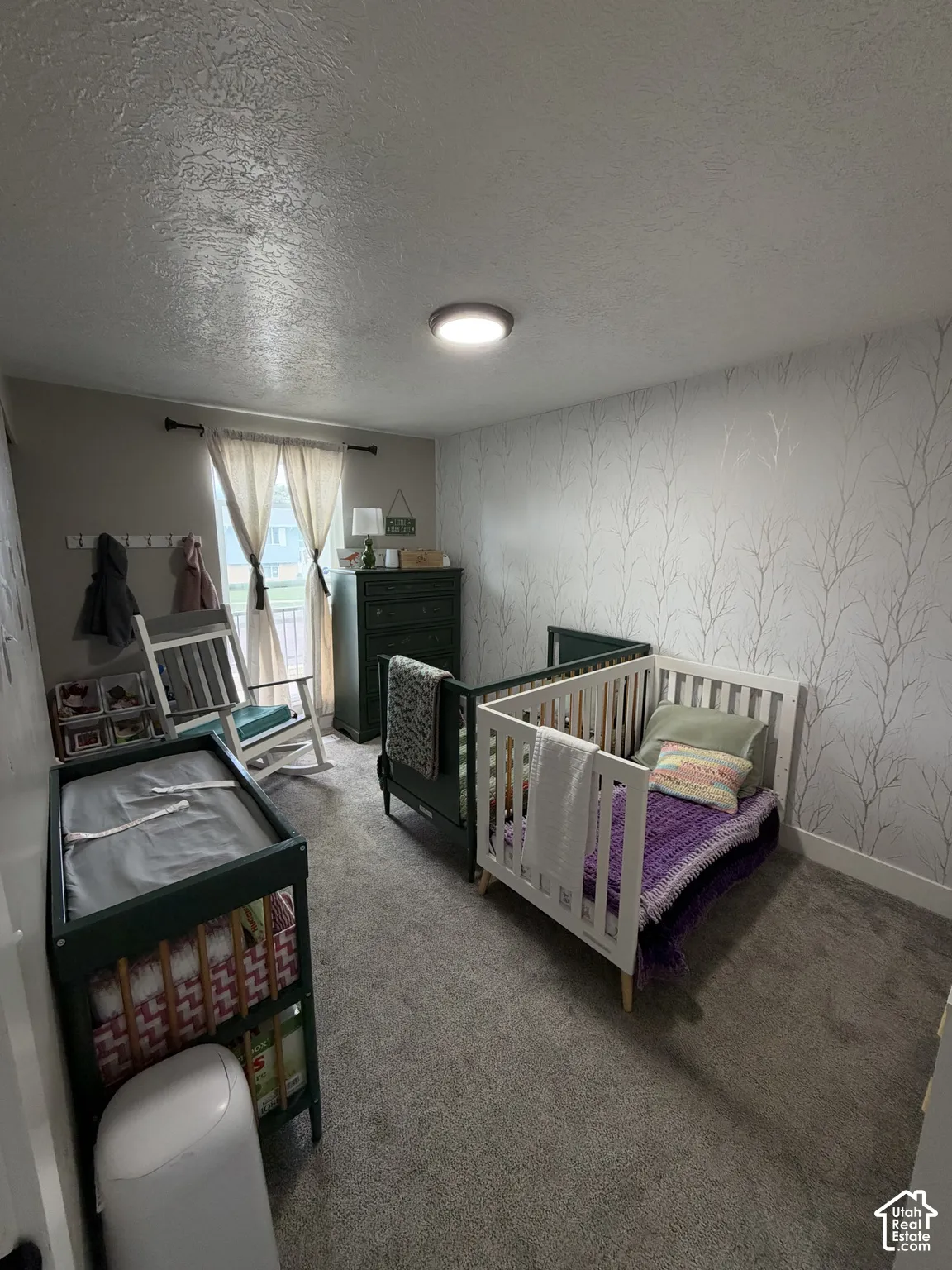 Bedroom featuring neutral wall-to-wall carpeting, textured wallpaper with a branch motif, and a flush-mount ceiling light fixture