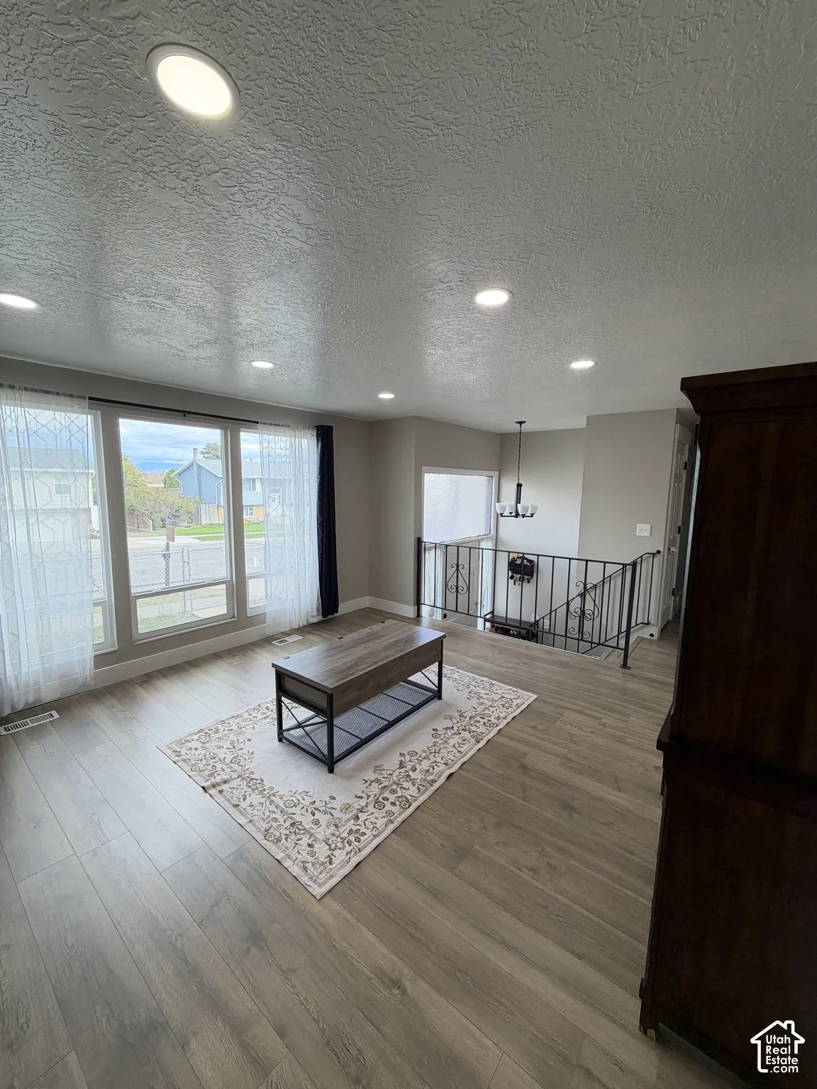 Open-concept interior featuring wood-finish flooring, recessed lighting, large picture windows, and decorative metal stair railing