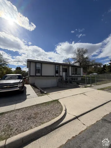 Split-level exterior featuring a painted masonry and siding facade, an attached garage, large picture windows, and a concrete driveway