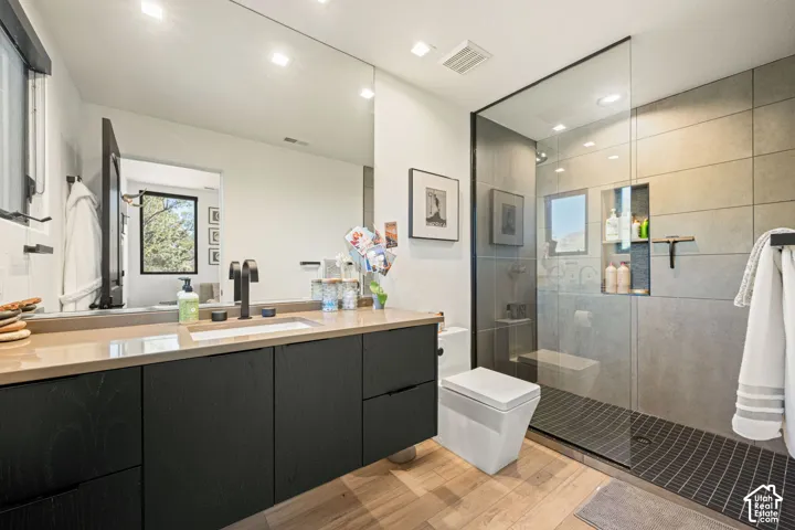 Floating vanity with a quartz countertop, matte black faucet, wall-to-wall mirror, walk-in shower with a glass panel enclosure, and wood-finish flooring