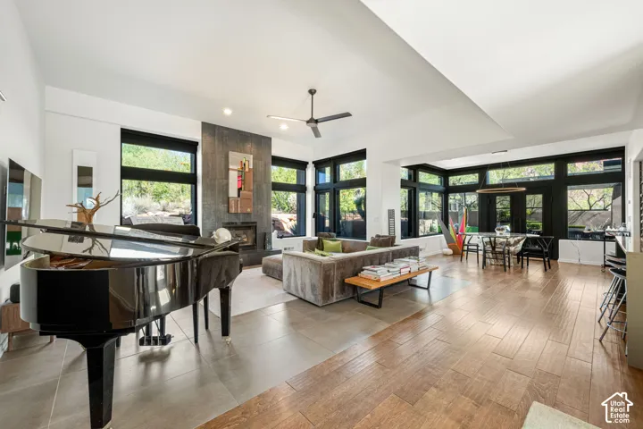 Open-concept living space featuring high ceilings, wood-finish tile flooring, a floor-to-ceiling dark stone fireplace surround, and expansive windows with black frames