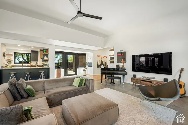 Open-concept living space featuring vaulted ceilings, oversized tile flooring, a matte black ceiling fan, and built-in kitchen cabinetry with a breakfast bar