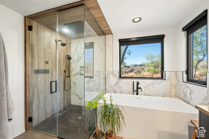 Walk-in shower featuring a frameless glass enclosure, wood-finish wall paneling, and matte black hardware, accompanied by a freestanding soaking tub with floor-mounted faucet and large-format tile surround