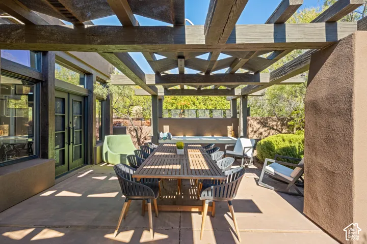 Outdoor patio featuring a wooden pergola, concrete flooring, dual-pane glass doors, and a built-in stucco wall