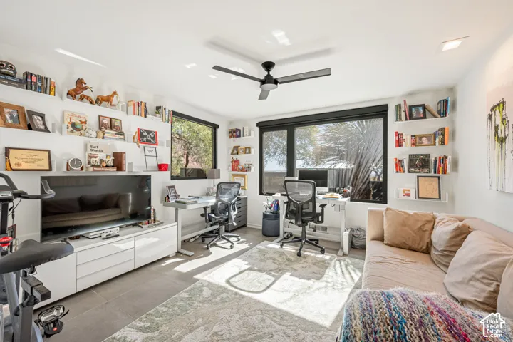 Room featuring matte black ceiling fan, large windows with black frames, tile flooring, and integrated white wall-mounted shelving units