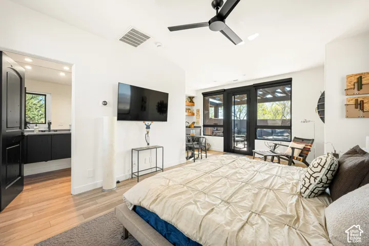 Bedroom featuring wood-finish flooring, a matte black ceiling fan, and black-framed windows with a glass door leading to a covered patio