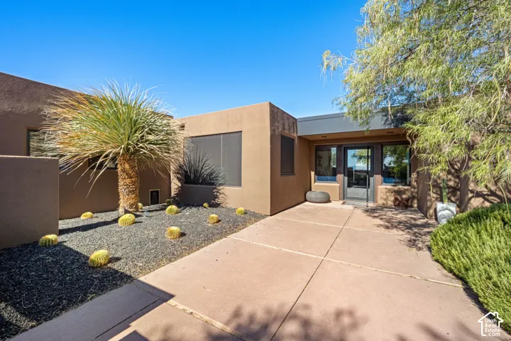 Stucco exterior featuring a concrete walkway, rock landscaping, native desert plantings, and a glass-paneled entry door