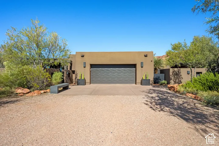 Stucco exterior with a textured finish, integrated multi-car garage, concrete driveway, and desert landscaping