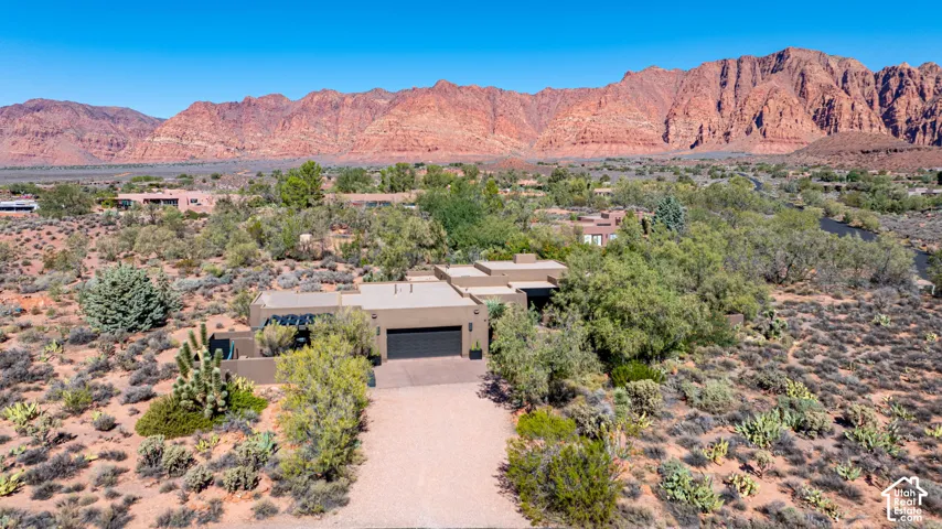 Stucco exterior residence with a multi-car garage, expansive gravel driveway, and desert landscaping set against a prominent red rock mountain backdrop