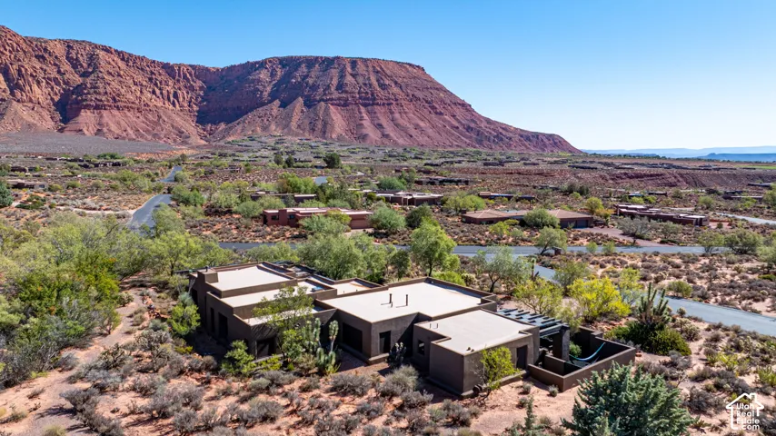 Contemporary flat-roof residence featuring stucco exterior walls, a private courtyard with integrated pergola, and desert landscaping set against a prominent red rock mountain backdrop