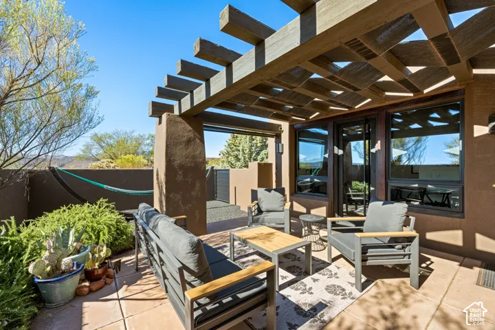 Covered patio featuring a wood-beam pergola, natural-finish stone flooring, stucco exterior wall, and dark-framed glass paneled door