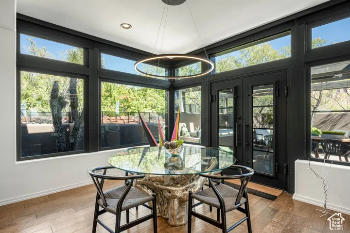 Floor-to-ceiling windows with black frames, wood-finish flooring, modern circular pendant lighting, and full-glass panel French doors