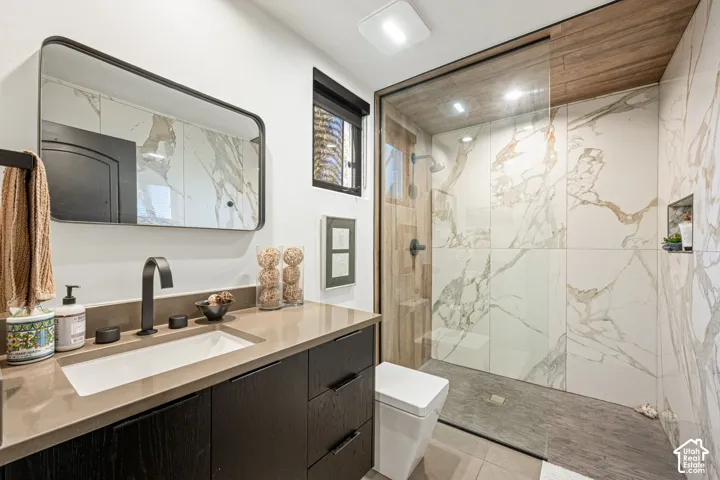 Bathroom featuring a dark wood-finish vanity with a solid-surface countertop, matte black fixtures, a wall-mounted rectangular mirror, and a walk-in shower with floor-to-ceiling tile, wood-finish ceiling, and a built-in recessed wall niche
