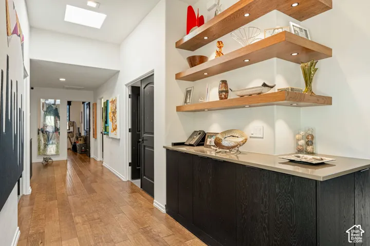 Hallway featuring wood-finish flooring, a skylight, and built-in cabinetry with a stone-finish countertop and integrated wood shelving with recessed lighting