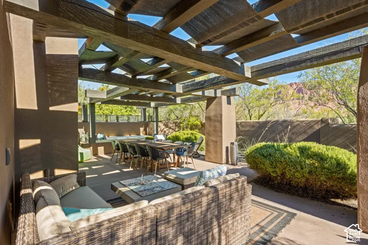 Covered patio featuring a timber-frame pergola, concrete flooring, stucco-finished support columns, and a masonry perimeter wall set against a mountain backdrop
