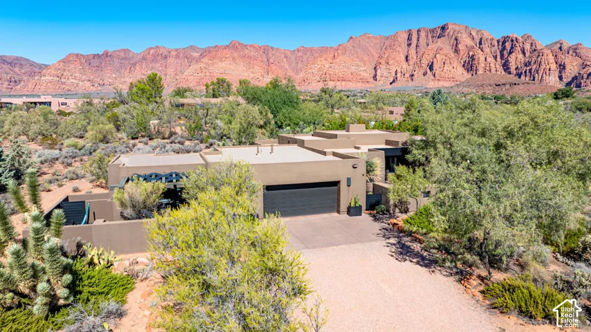 Single-level residence with stucco exterior, attached garage, integrated pergola, and desert landscaping, featuring a prominent red rock mountain backdrop