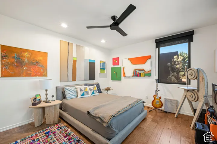 Room featuring wood-finish flooring, a matte black ceiling fan, recessed lighting, and a window with a black roller shade