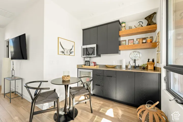 Wet bar featuring matte black cabinetry, solid-surface countertops, built-in microwave, under-counter beverage refrigerator, and open wood shelving