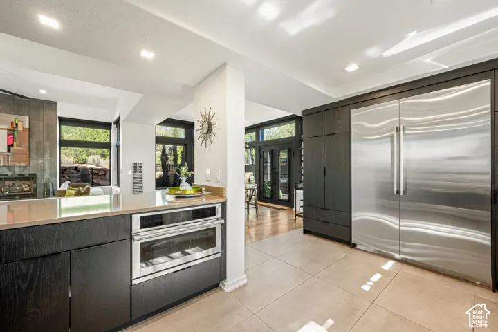 Kitchen featuring dark wood cabinetry, integrated stainless steel refrigeration, built-in stainless steel oven, stone-finish countertops, and large-format tile flooring