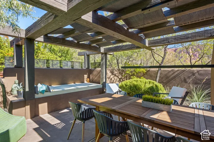 Outdoor patio featuring a timber-frame pergola, built-in masonry bench seating, concrete paving, and natural rock formation backdrop