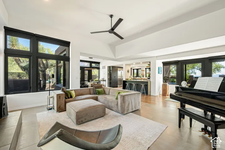 Open-concept interior featuring high vaulted ceilings, expansive black-framed windows, large-format tile flooring, a matte black ceiling fan, and a built-in kitchen island with a stone-surface countertop