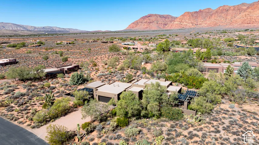 Single-level desert residence featuring a flat roofline, attached garage, integrated pergolas, and native landscape, set against a prominent mountain backdrop