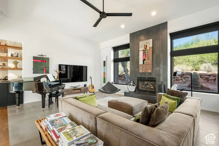 Living area featuring a floor-to-ceiling fireplace with dark tile surround, large windows, recessed lighting, a modern ceiling fan, and built-in shelving with integrated lighting